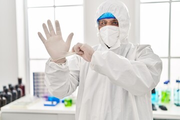 Young latin man scientist wearing covid protection uniform and gloves at laboratory