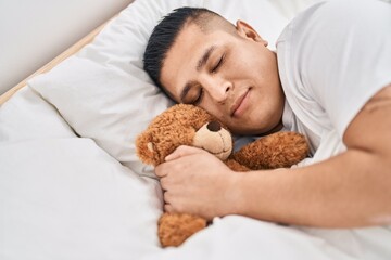 Obraz na płótnie Canvas Young latin man hugging teddy bear lying on bed sleeping at bedroom