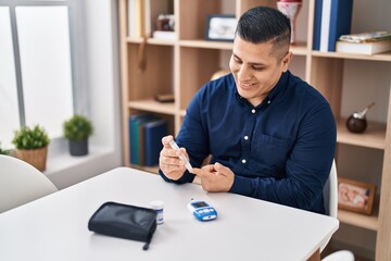 Young latin man measuring glucose sitting on table at home