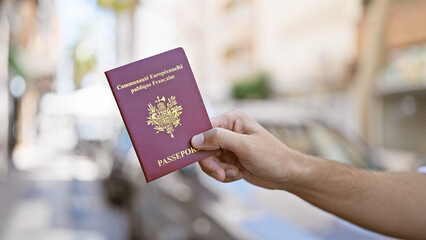 Hand holding french passport on sunlit city street, suggesting urban travel or immigration theme.