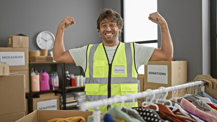 A cheerful man flexes his muscles proudly in a donation center filled with boxes and clothing.