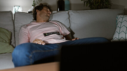 Relaxed young man sleeping on a couch in a cozy living room, holding a remote