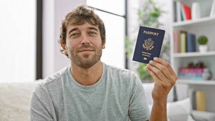 Happy young man lounging on his sofa at home, grinning ear to ear, flaunting his passport of the...