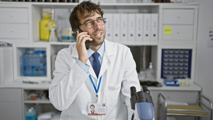 Handsome young blond scientist, confidently smiling and talking on his smartphone, tying loose ends...