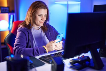 Young beautiful plus size woman streamer using computer and smartphone at gaming room