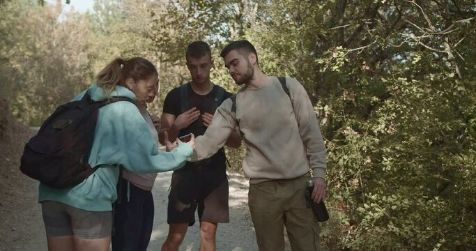 Group of sports friends standing on a trail in the forest and watching something on the phone. They are hiking and enjoying the day off surrounded by beautiful natural environment.