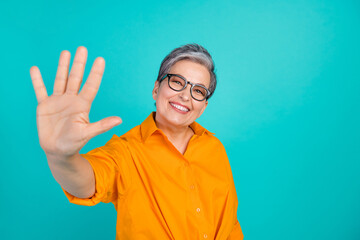 Photo of optimistic pensioner woman grey haired grandmother raise arm towards you saying hello isolated on aquamarine color background