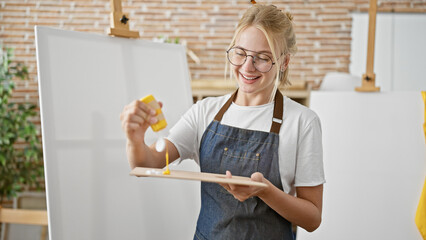 Young blonde woman artist smiling confident pouring color on palette at art studio