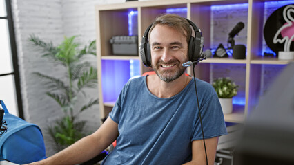 A smiling middle-aged hispanic man with a beard wearing headphones in a gaming room at home