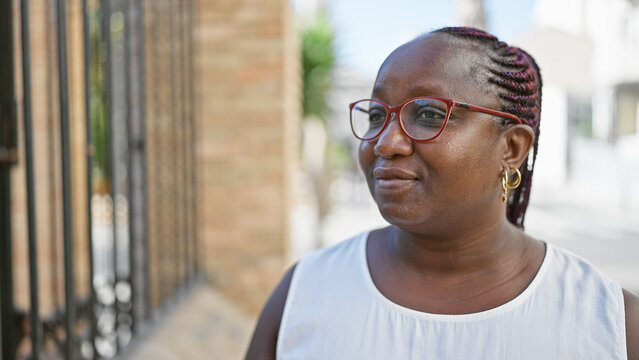 Cool plus size african american woman in glasses, with braids, casting a serious expression while looking to the side on a sunny urban street.