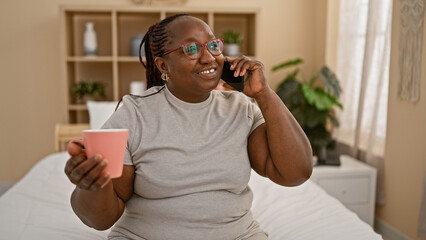 Confident african american woman with braids and glasses, sipping coffee as she chats on her...
