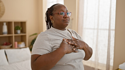 African american woman calmly breathing with hands on chest, awake in her bedroom, embracing the...