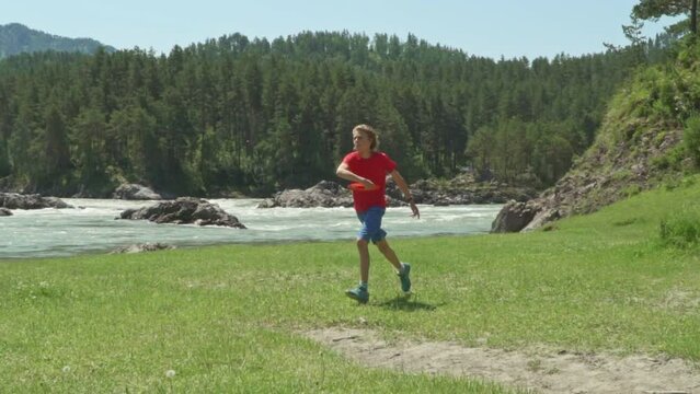 Cute little children playing with frisbee outdoors on sunny day. Against the backdrop of mountains, on the coast of a mountain river.
Slow motion. Young Boys throwing a red frisbee disk. 