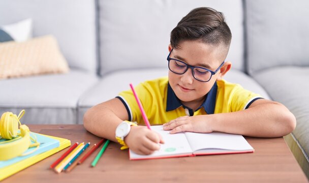 Adorable hispanic boy drawing on book sitting on floor at home