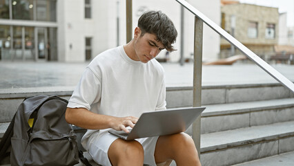 Cool young hispanic teenager, a smart university student engrossed in online study on laptop while...