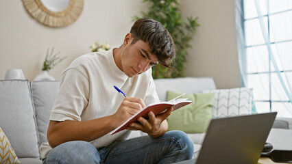 Young hispanic teenager engrossed in studying on his notebook, sitting comfortably on a sofa at...