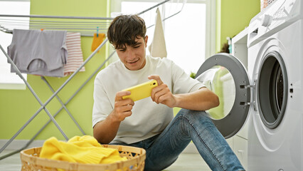 Caught in the thick of housekeeping, young hispanic teenager engages in serious gaming, waiting by...