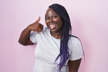 Young african woman standing over pink background smiling doing phone gesture with hand and fingers like talking on the telephone. communicating concepts.