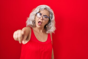 Middle age woman with grey hair standing over red background pointing displeased and frustrated to...