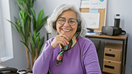 Smiling grey-haired woman in headset sitting at office represents professionalism and approachability.
