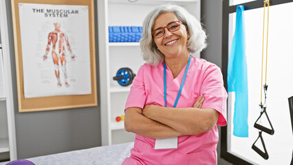 Confident woman healthcare professional with arms crossed stands in a rehabilitation clinic interior.