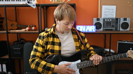 A concentrated man playing electric guitar in a cozy music studio with orange walls and recording...