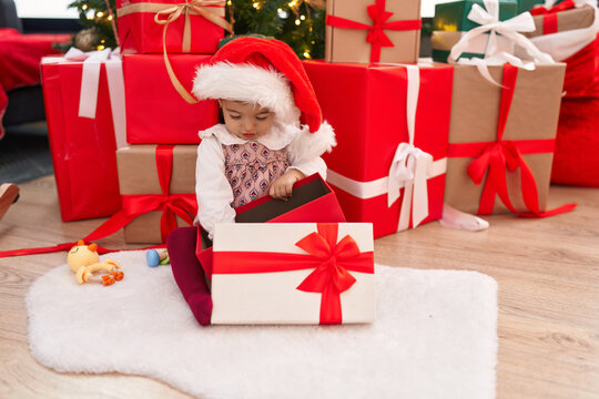 Adorable blonde toddler unpacking gift sitting by christmas tree at home