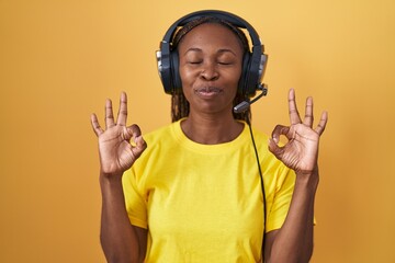 African american woman listening to music using headphones relax and smiling with eyes closed doing meditation gesture with fingers. yoga concept.