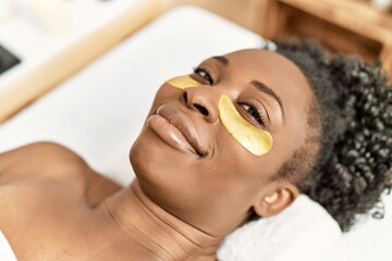 African american woman lying on massage table having eye mask treatment at beauty salon