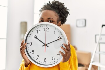 African american woman covering mouth with clock at new home