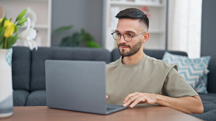 Young hispanic man using laptop sitting on floor at home
