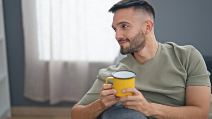 Young hispanic man drinking coffee sitting on sofa at home