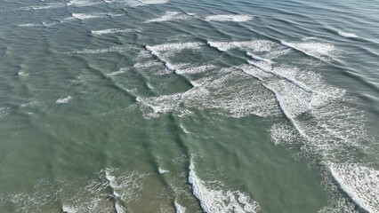 Drone view looking down on ocean beach coastline with waves and sunlight in early morning of day