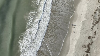 Drone view looking down on ocean beach coastline with waves and sunlight in early morning of day