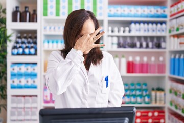 Middle age brunette woman working at pharmacy drugstore tired rubbing nose and eyes feeling fatigue and headache. stress and frustration concept.