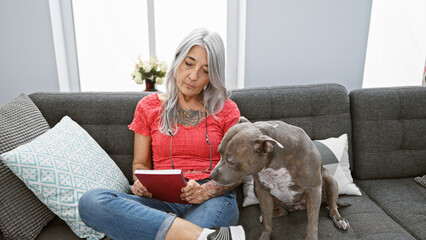 Relaxed middle age woman, a grey-haired bibliophile, snuggled up with her loyal dog, comfortably...