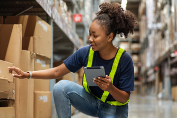Young black African American woman holding a tablet sits checking inventory and checking orders from customers, picking up boxes from shelves to deliver documents to customers in warehouse wholesale 