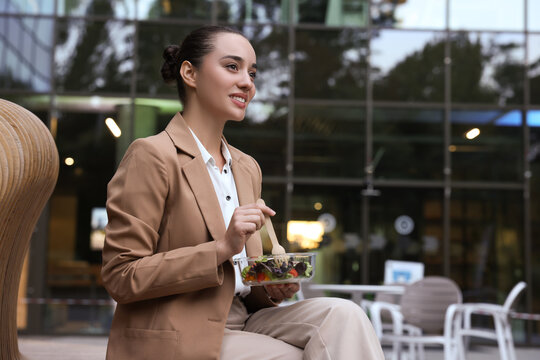 Happy Young Businesswoman Eating Lunch On Bench Outdoors