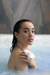 Beautiful woman with orchid flower relaxing in spa swimming pool