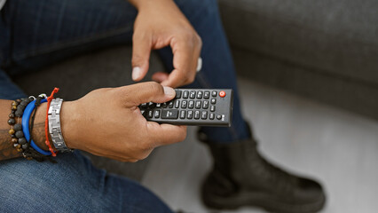 African american man in casual attire holding a remote control at home, symbolizing leisure and...
