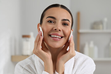 Beautiful woman removing makeup with cotton pads indoors