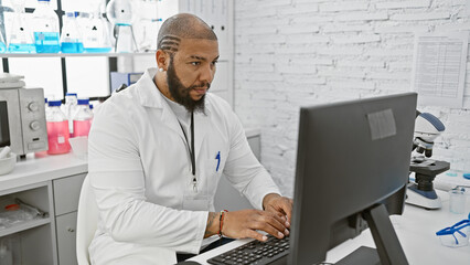 African man in white lab coat working on computer in modern laboratory setting