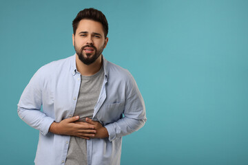 Young man suffering from stomach pain on light blue background. Space for text