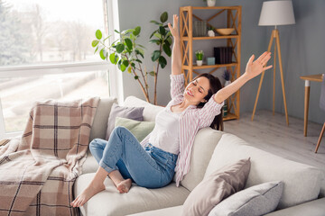 Full size portrait of nice cheerful girl sit couch closed eyes raise arms spend pastime spacious...
