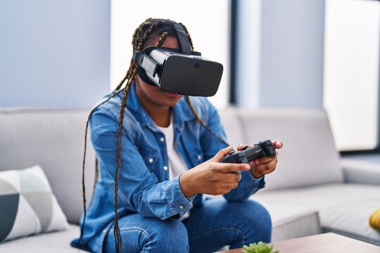 African american woman playing video game using virtual reality glasses and joystick at home