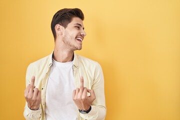 Young hispanic man standing over yellow background showing middle finger doing fuck you bad...