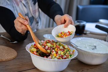 The wife fills a salad bowl with a large bowl of yogurt next to it to provide the guests with what...