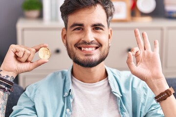 Young hispanic man with tattoos holding tether cryptocurrency coin doing ok sign with fingers,...