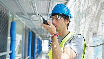 Young hispanic man architect talking on walkie-talkie at construction place