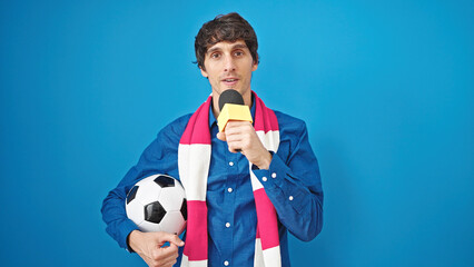 Young hispanic man soccer reporter working using microphone holding football ball over isolated...